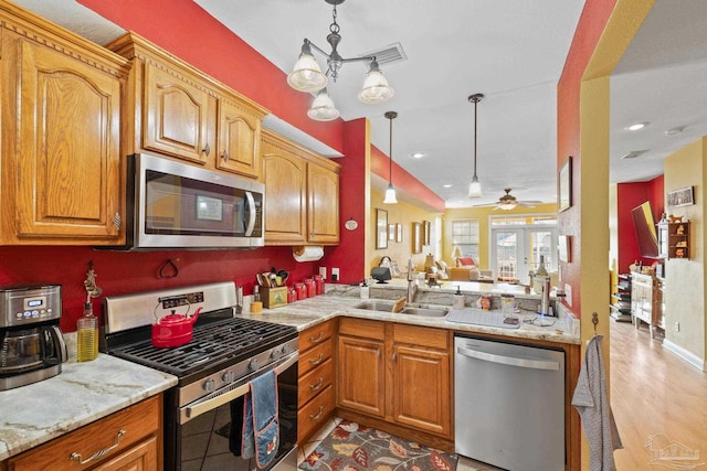 kitchen featuring light stone counters, stainless steel appliances, sink, and hanging light fixtures