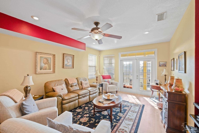 living room with french doors, ceiling fan, light colored carpet, and a textured ceiling