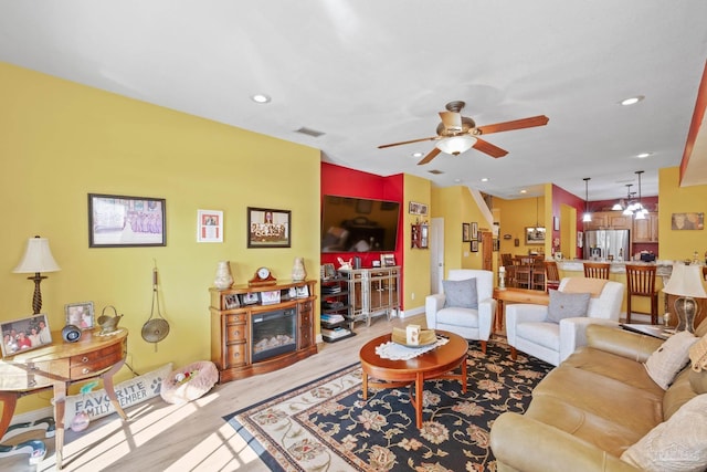 living room with ceiling fan with notable chandelier and light wood-type flooring