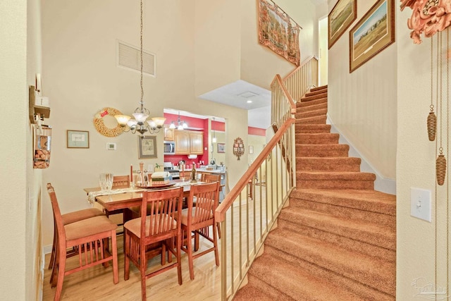 staircase with a towering ceiling, wood-type flooring, and a notable chandelier