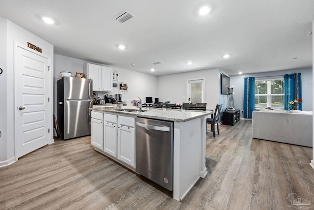 4616 Honor Guard Way, Crestview, FL 32539 - kitchen with stainless steel appliances, white cabinets, a kitchen island with sink, light wood-style flooring, and light stone countertops