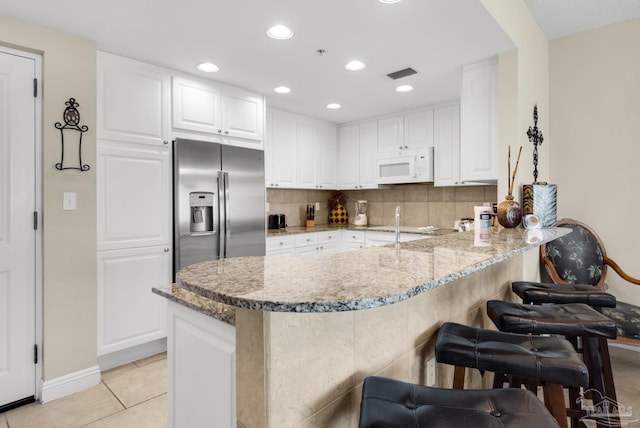 kitchen with a kitchen bar, kitchen peninsula, white cabinets, and stainless steel refrigerator with ice dispenser