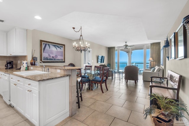 kitchen featuring dishwasher, dark stone counters, white cabinets, a water view, and sink