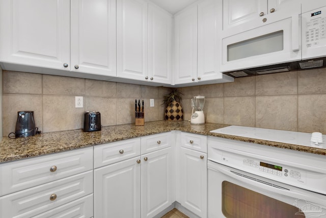 kitchen with backsplash, white cabinets, dark stone counters, and white appliances