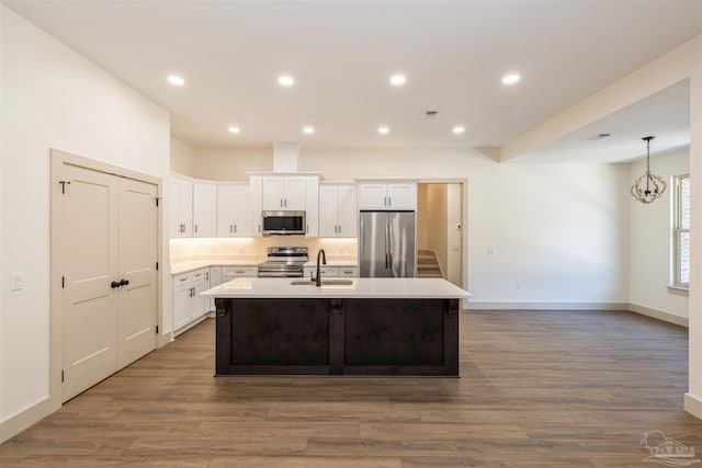 kitchen featuring stainless steel appliances, light countertops, a kitchen island with sink, white cabinets, and a sink