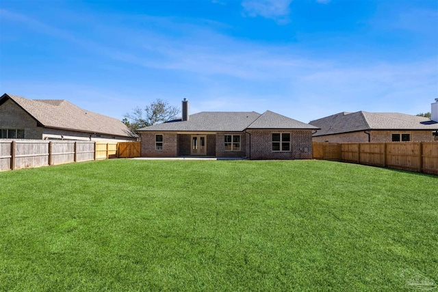 rear view of property featuring brick siding, a lawn, a chimney, and a fenced backyard