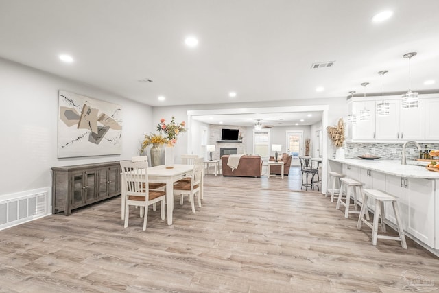 dining room with a large fireplace, light hardwood / wood-style floors, ceiling fan, and sink