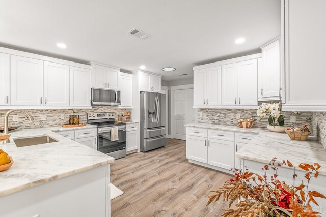 kitchen with light stone counters, stainless steel appliances, white cabinetry, and sink