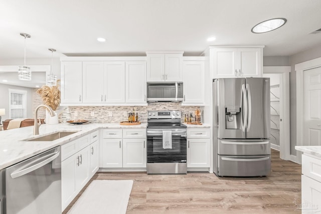 kitchen featuring appliances with stainless steel finishes, light wood-type flooring, sink, pendant lighting, and white cabinetry