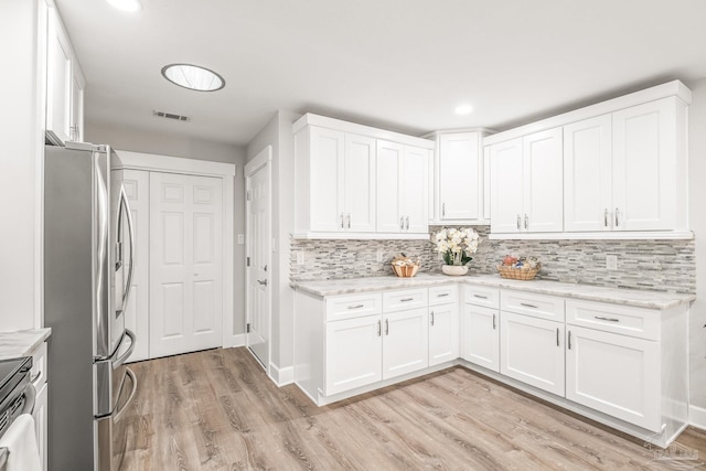 kitchen featuring tasteful backsplash, light stone counters, stainless steel appliances, white cabinets, and light hardwood / wood-style floors