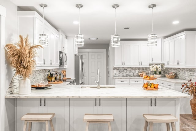 kitchen featuring white cabinetry, sink, stainless steel appliances, a kitchen breakfast bar, and light stone counters