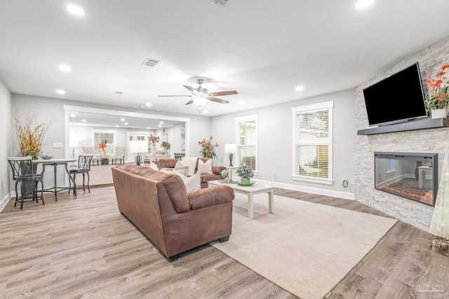 living room featuring a stone fireplace, ceiling fan, and light hardwood / wood-style flooring