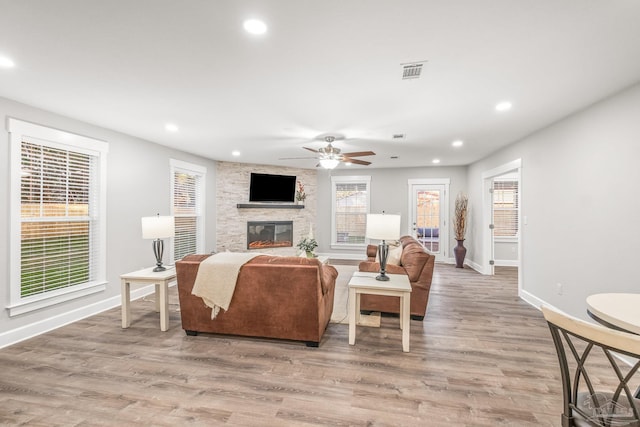 living room with light wood-type flooring, a stone fireplace, and a healthy amount of sunlight