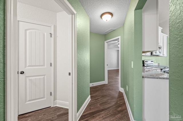 hallway with a textured wall, a textured ceiling, dark wood finished floors, baseboards, and visible vents