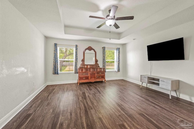 unfurnished living room with a ceiling fan, a tray ceiling, dark wood finished floors, and baseboards