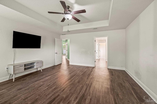 unfurnished living room with visible vents, dark wood-style flooring, baseboards, a tray ceiling, and a ceiling fan