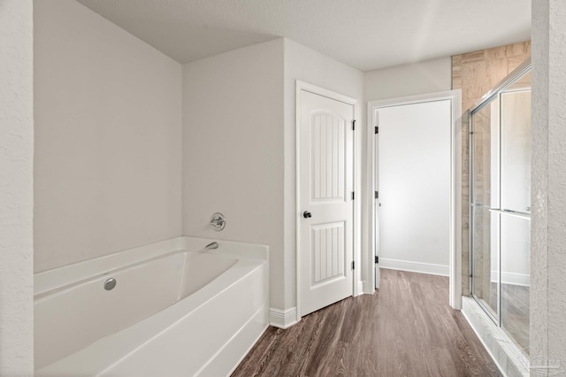 full bath featuring a garden tub, baseboards, wood finished floors, and a shower stall