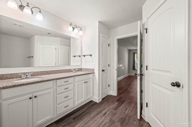 bathroom featuring a textured ceiling, visible vents, a sink, and wood finished floors