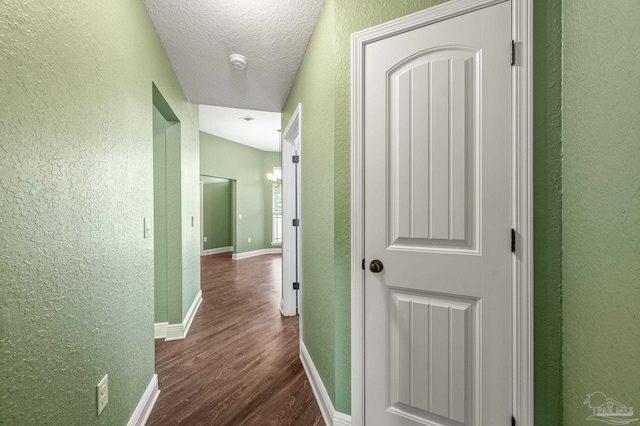 hall with dark wood-type flooring, a textured ceiling, a textured wall, and baseboards