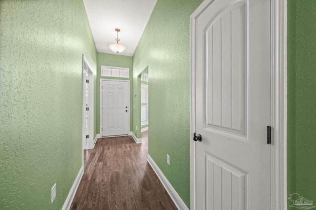 hallway with dark wood-type flooring, a textured wall, and baseboards