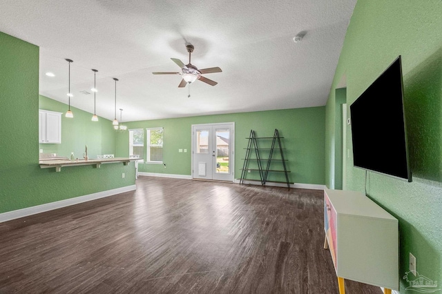 unfurnished living room featuring baseboards, dark wood-type flooring, a textured ceiling, a ceiling fan, and vaulted ceiling