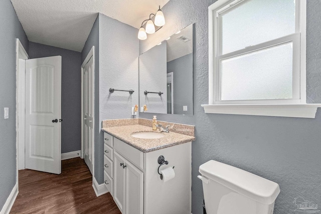 bathroom featuring a textured wall, vanity, toilet, wood finished floors, and visible vents