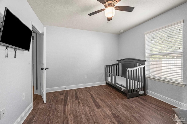 unfurnished bedroom with a ceiling fan, baseboards, a crib, and wood finished floors