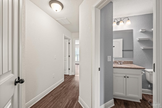 corridor with a sink, baseboards, a textured wall, and dark wood-style flooring