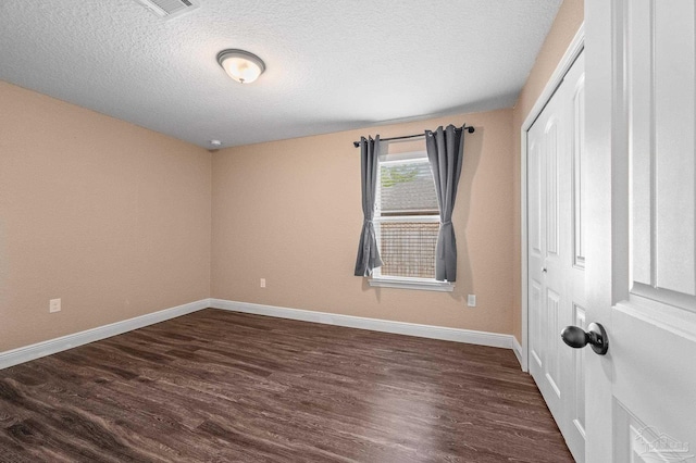 spare room with a textured ceiling, dark wood finished floors, and baseboards