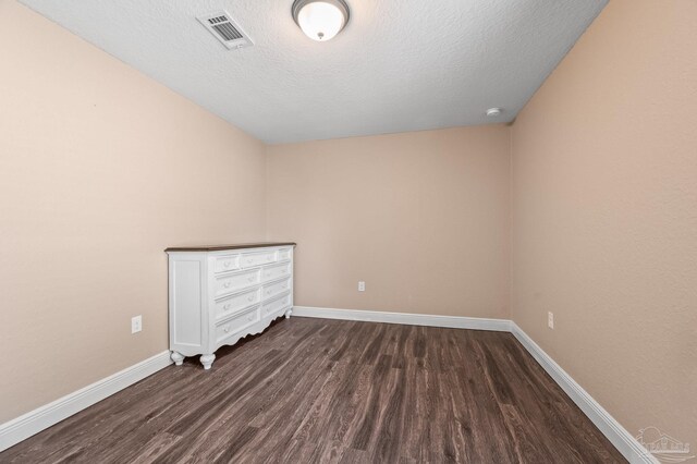 unfurnished room with baseboards, dark wood-style flooring, a textured ceiling, and visible vents