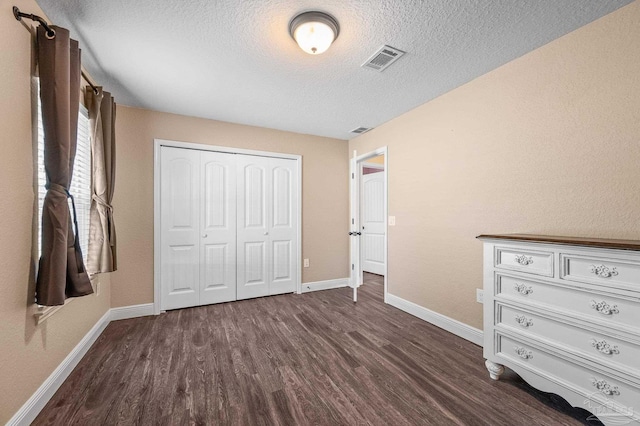 unfurnished bedroom with dark wood-style flooring, a textured ceiling, visible vents, and baseboards