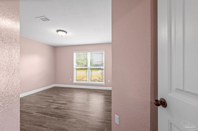 empty room with visible vents, a textured wall, baseboards, a textured ceiling, and dark wood finished floors