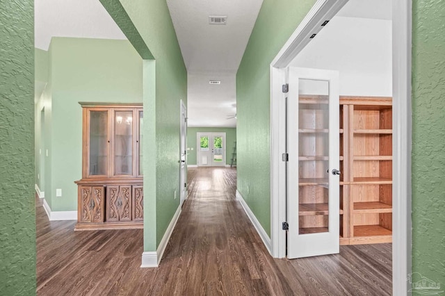 hallway with baseboards, a textured wall, visible vents, and wood finished floors