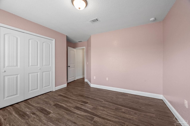 unfurnished bedroom with dark wood-style flooring, a textured ceiling, visible vents, baseboards, and a closet