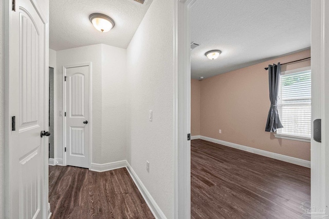 hallway with baseboards, a textured ceiling, visible vents, and wood finished floors