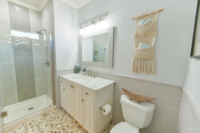 bathroom with vanity, toilet, ornamental molding, tile walls, and a shower with shower door