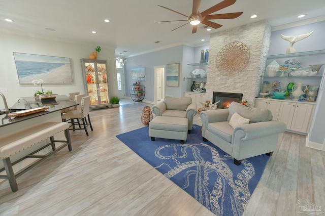 living room with a stone fireplace, built in features, ornamental molding, and light hardwood / wood-style flooring