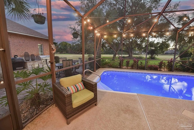 pool at dusk with glass enclosure, area for grilling, and a patio