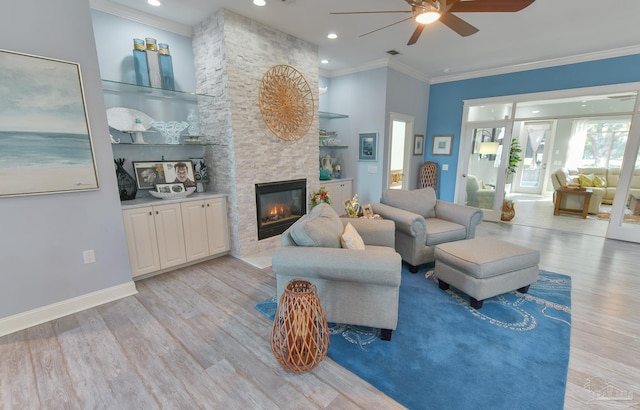 living room featuring light wood-type flooring, ceiling fan, crown molding, built in features, and a stone fireplace