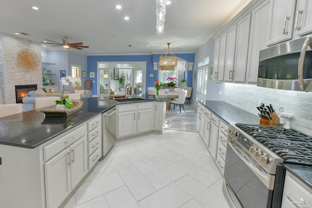 kitchen featuring sink, stainless steel appliances, a stone fireplace, pendant lighting, and ornamental molding