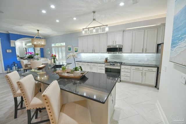 kitchen featuring a kitchen island with sink, sink, hanging light fixtures, appliances with stainless steel finishes, and a kitchen bar