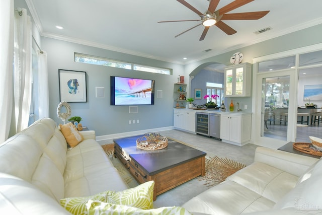 living room with bar area, crown molding, ceiling fan, and beverage cooler