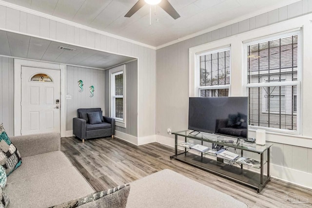 living room with ceiling fan, hardwood / wood-style floors, wood walls, and crown molding