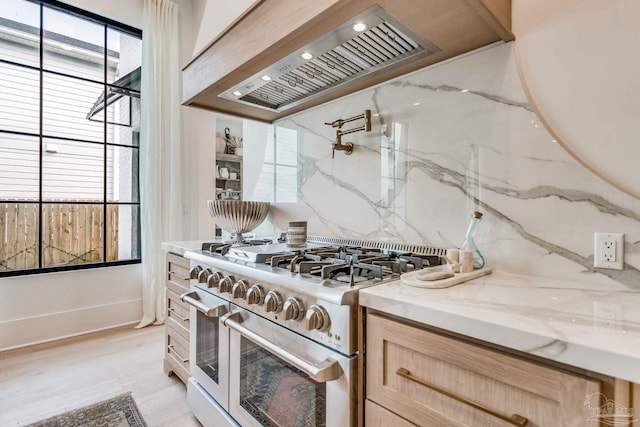 kitchen with tasteful backsplash, premium range hood, light brown cabinetry, stainless steel range, and light hardwood / wood-style flooring