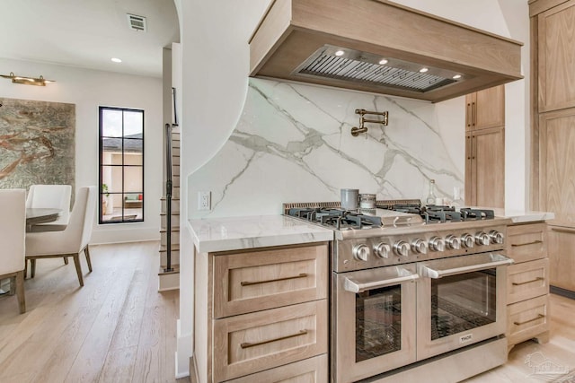 kitchen with double oven range, light brown cabinetry, light wood-type flooring, and tasteful backsplash