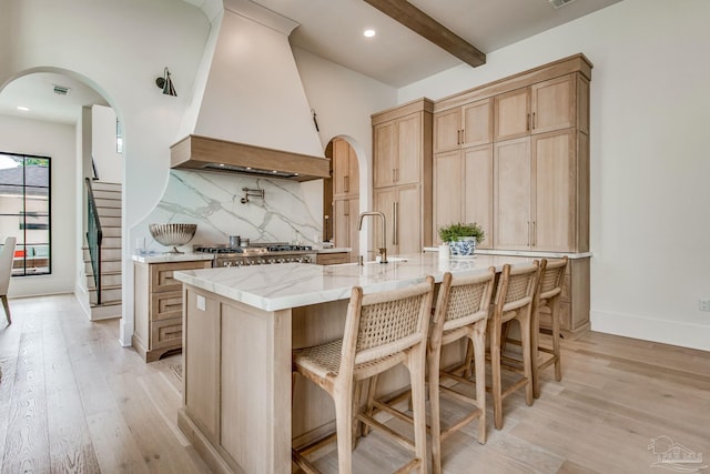 kitchen with a center island with sink, decorative backsplash, light hardwood / wood-style flooring, light brown cabinetry, and premium range hood