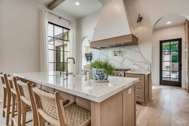 kitchen with custom exhaust hood, a kitchen island with sink, and a wealth of natural light