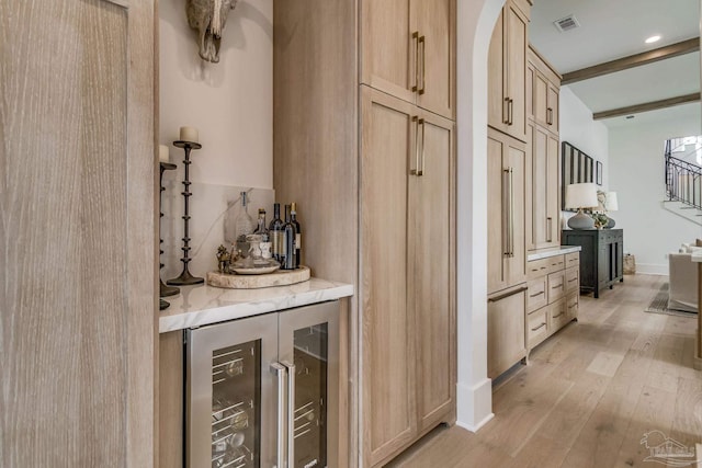 bar featuring light brown cabinets, beam ceiling, beverage cooler, and light wood-type flooring