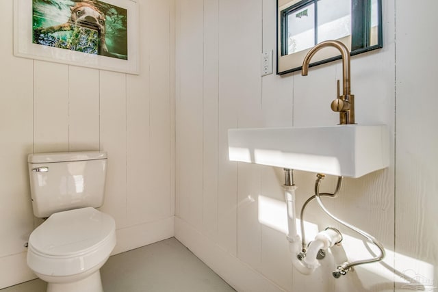 bathroom featuring toilet, wooden walls, and sink