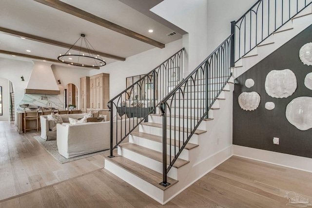 stairway featuring hardwood / wood-style flooring, beam ceiling, and an inviting chandelier